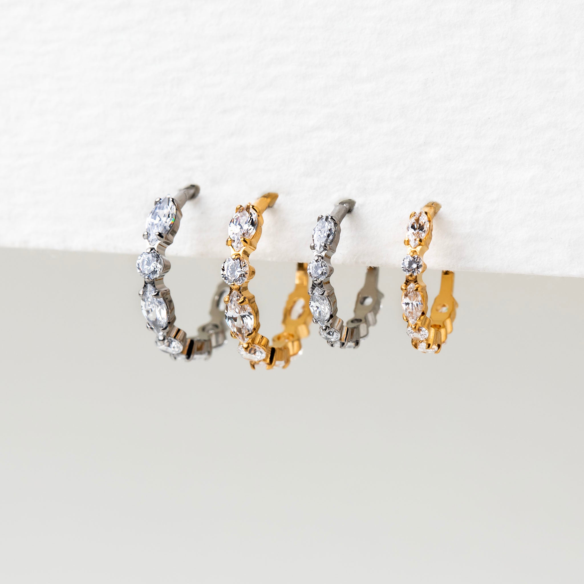 An assortment of silver and gold hoop earrings with clear marquise and round stones in an alternating pattern.